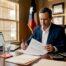Lubbock Texas insurance agent in navy blazer reviewing Texas Commercial Umbrella Policy at mahogany desk with Texas flag behind.