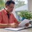 Texas Homeowner in coral shirt and glasses reading an insurance binder document at a bright granite kitchen counter.
