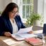 Texas independent insurance agent in navy blazer reviewing a client policy binder at a light wood desk in a bright Texas home office.