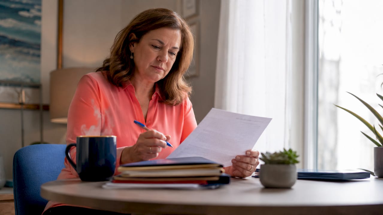 Woman in coral blouse reviewing a third-party auto liability policy in Texas, a document at a wood table in a warm home office.