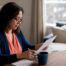 Small business owner in navy cardigan reviewing a Texas commercial insurance quote at a wood dining table with a notebook.