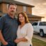 West Texas couple stands in front of brick suburban Lubbock home with white pickup at golden hour